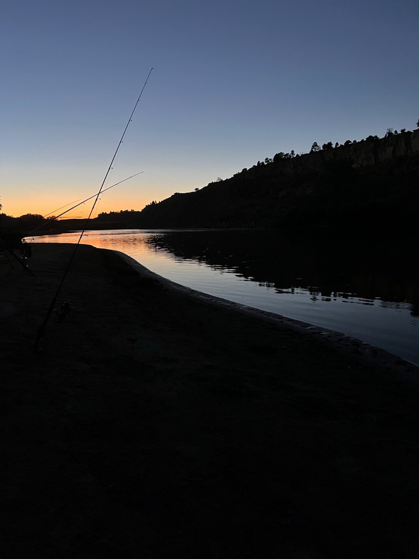 Fishing rods silhouetted against a sunset riverbank