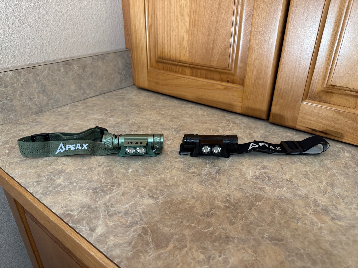 Two PEAX headlamps side by side — the olive green-mode lamp and the black red-mode lamp